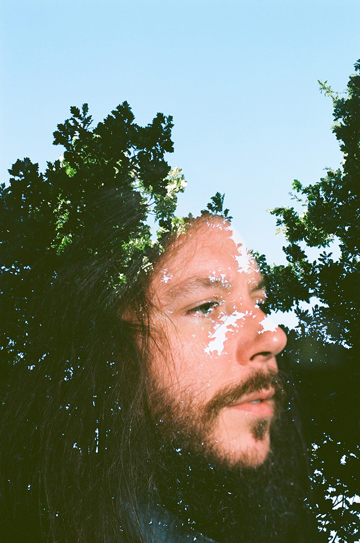 A double exposure portrait of Noah Fagan against trees and a sky